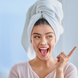 woman with hair in a towel and lotion on her nose