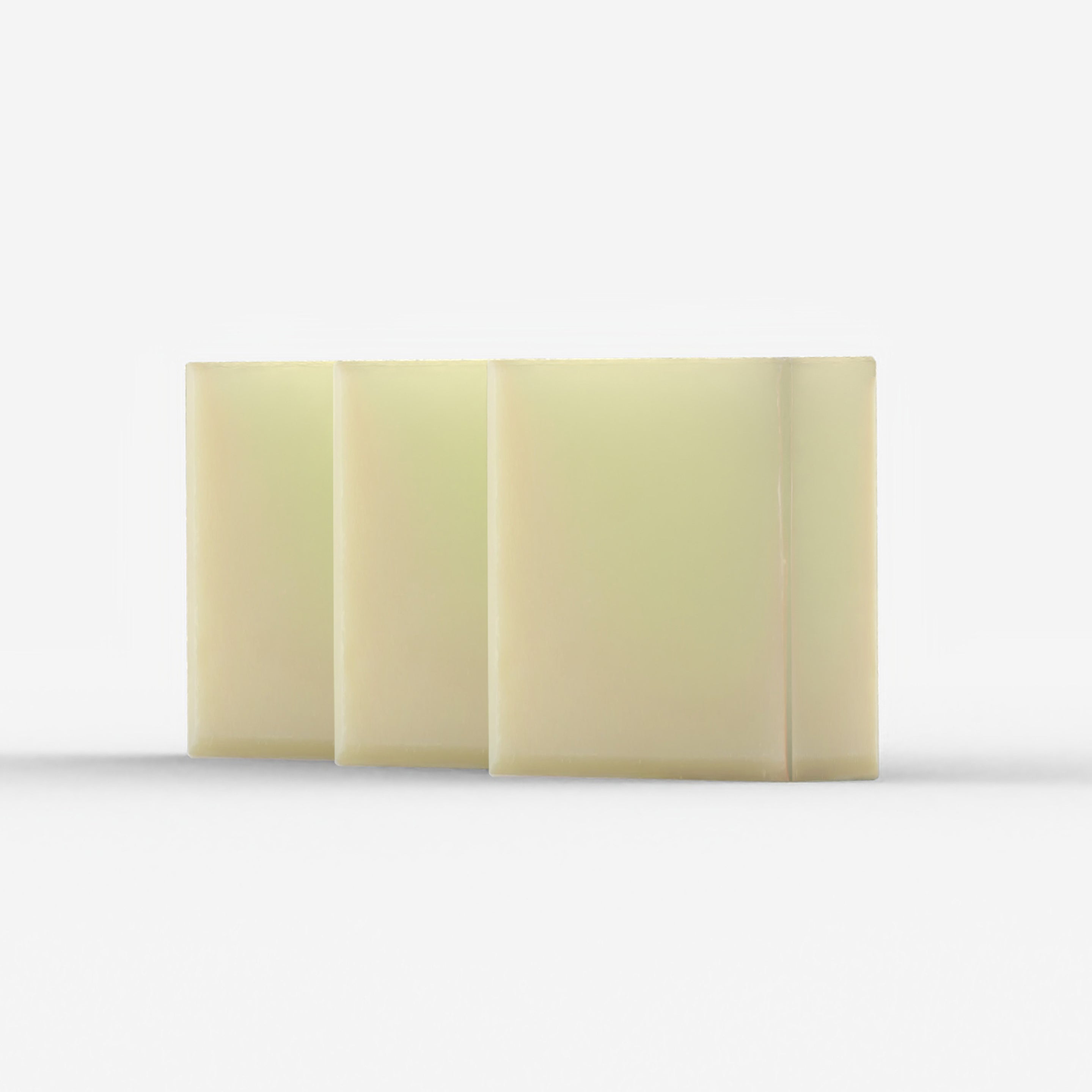 Three large, creamy white bars of tallow soap are stacked closely together, their smooth surfaces glowing with a gentle sheen, reminiscent of pure and natural skincare products.