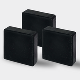 Three identical deep blue, almost slate-colored, charcoal tallow soap bars are aligned neatly against a light background. Their rustic texture is highlighted, with the natural variations in their handmade surface visible, conveying an artisanal and organic charm. Each bar's edges are softened, indicating a gentle use over time.