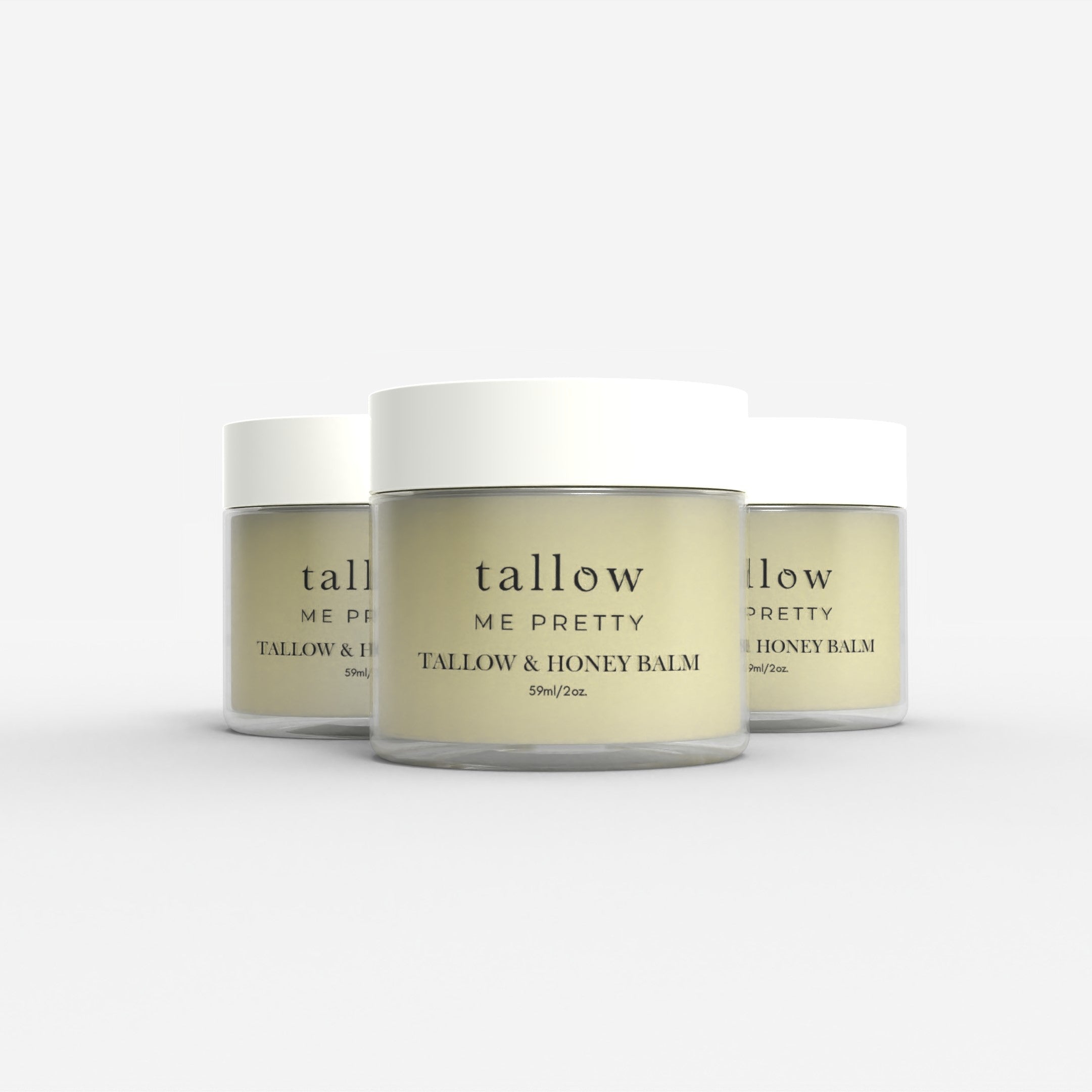 Three jars of 'Tallow Me Pretty Tallow & Honey Balm' are aligned against a white background, showcasing the product's uniform and elegant design. Each jar has a clean, white lid with the brand's signature simple typography on a golden-hued label that wraps around the container. The smooth, creamy appearance of the balm is visible through the clear glass, reflecting its natural and organic ingredients.