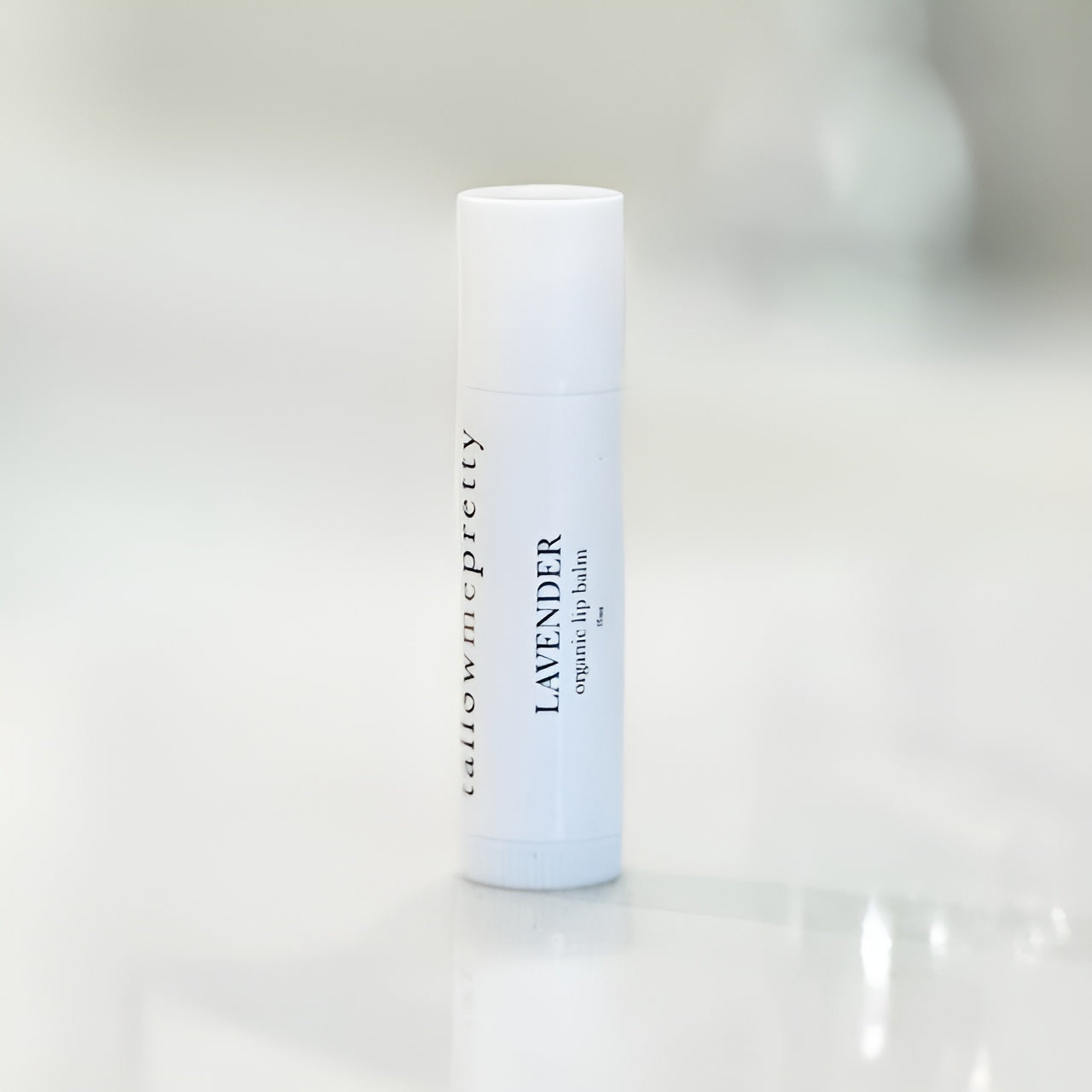 A Tallow Me Pretty Lavender Organic Lip Balm in a white, roll-up tube displayed on a glossy white surface. The tube's label is printed in elegant black typography, highlighting the organic and natural qualities of the product.