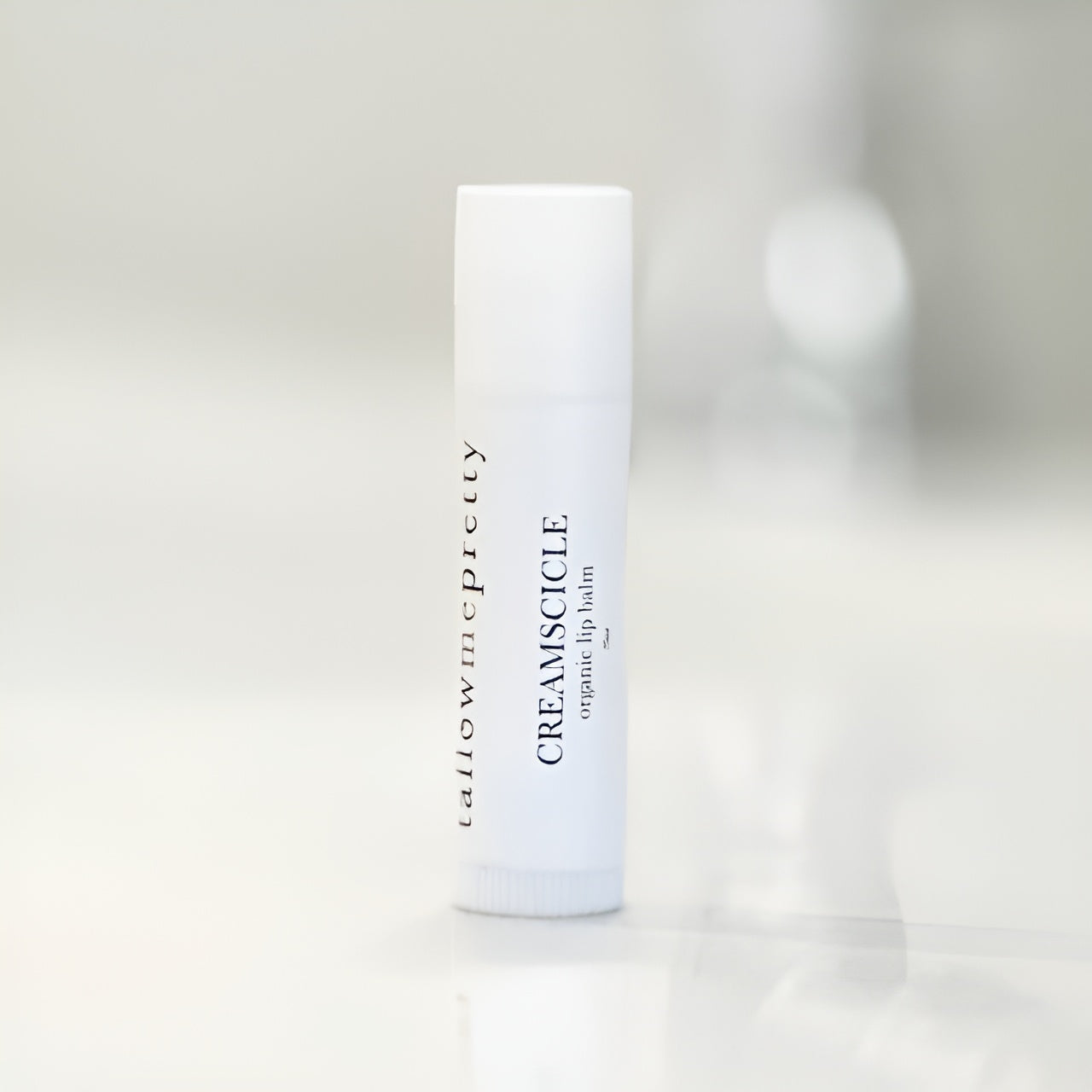 Product shot of Tallow Me Pretty's Creamsicle Organic Lip Balm, poised on a clean, soft-lit background, emphasizing the elegant and simple packaging, ready to provide soothing tallow-based lip care.